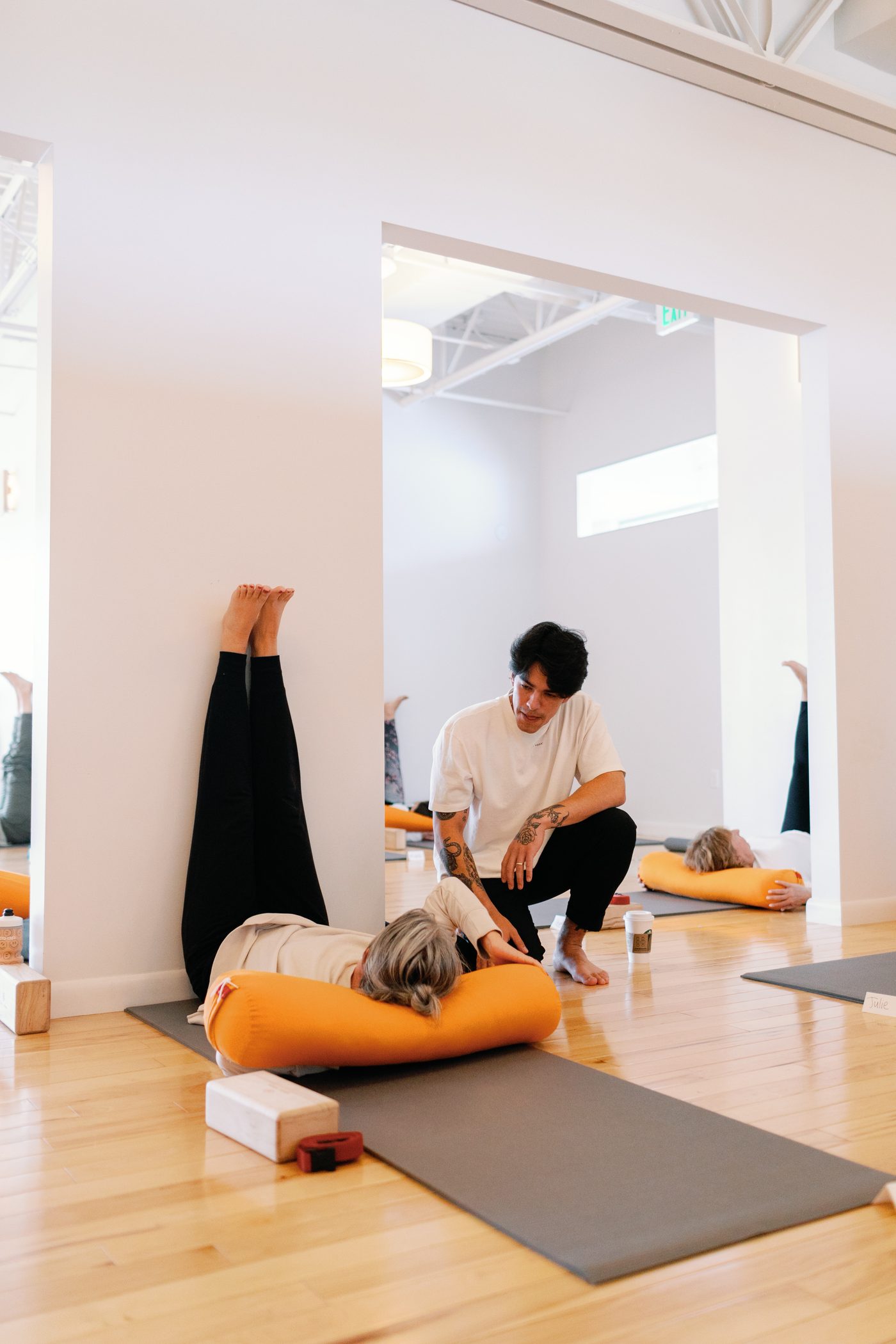Ravi Kaiut kneeling beside a student working with an orange bolster